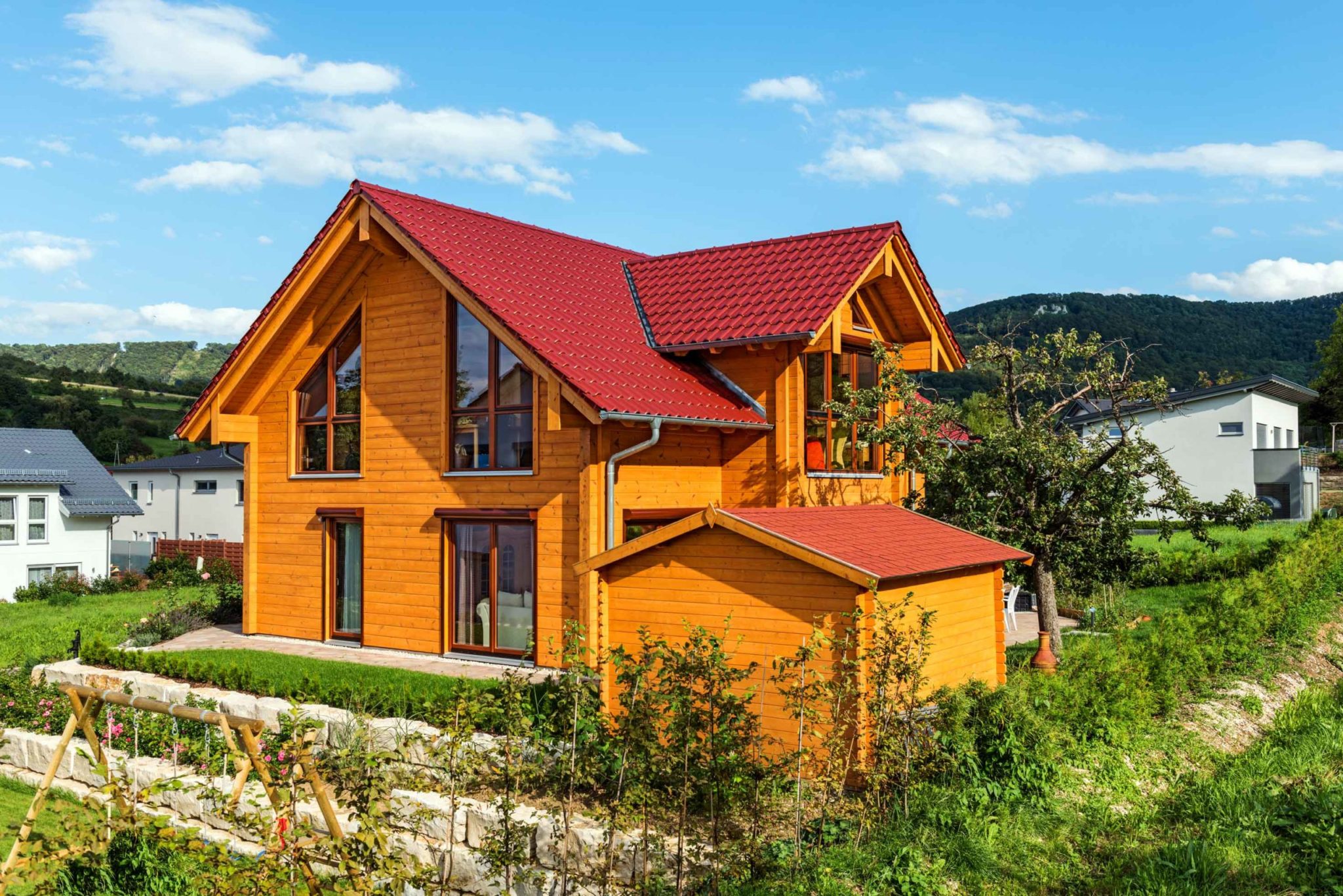 Landhaus aus Holz von Fullwood mit rotem Satteldach und naturbelassener Kiefernholzfassade in grüner Landschaft